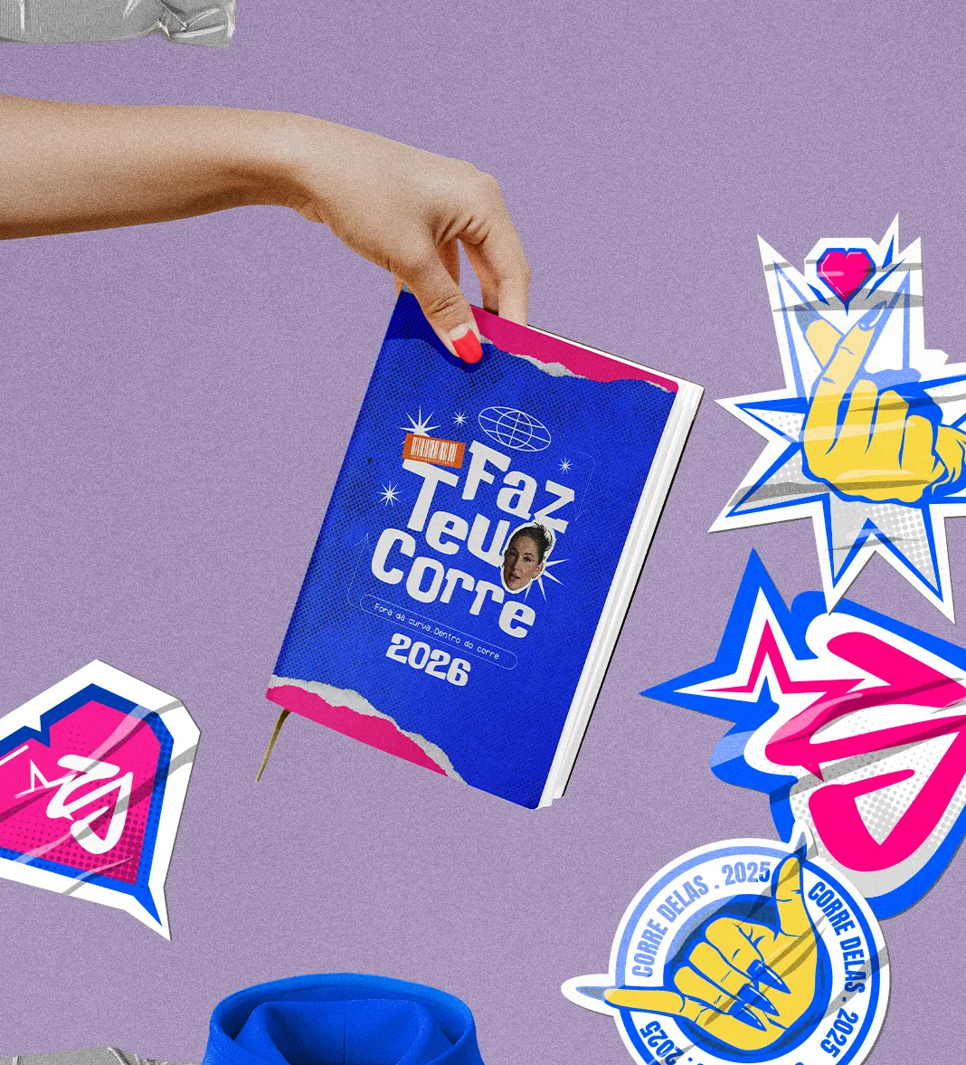 Mão segurando a agenda 2026 azul com o lettering Faz teu corre, cercada de adesivos sobre fundo lilás